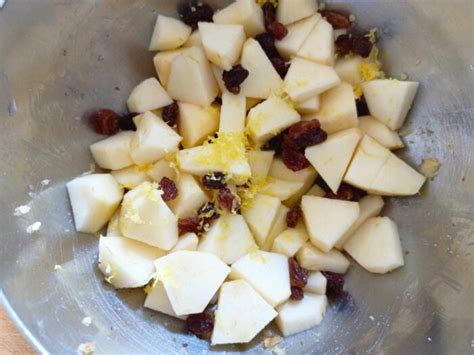Una ciotola con mele a tocchetti, zucchero, cannella, scorza di limone, uvetta e frutta secca, pronta per essere mescolata.
