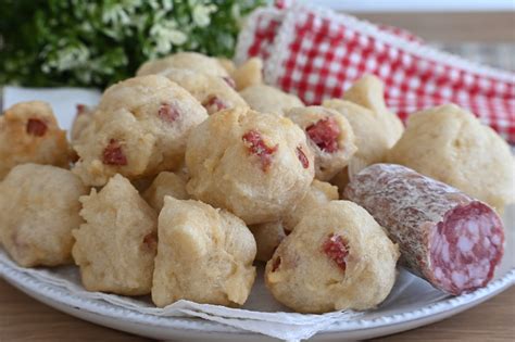 Un piatto di frittelle al salame dorate e croccanti, disposte su un vassoio, con una ciotolina di salsa in accompagnamento