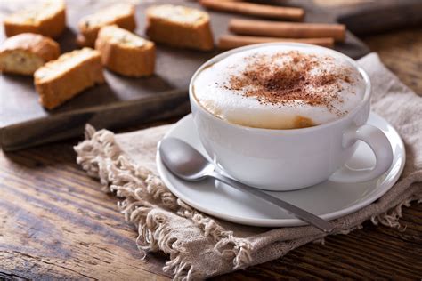 Un primo piano di un cappuccino con schiuma artistica e un assortimento di brioches in un cestino.