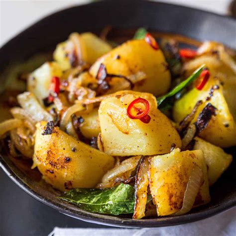 Una ciotola di patate Ala Thel Dala dorate e speziate, guarnite con foglie di curry fresche e peperoncino.