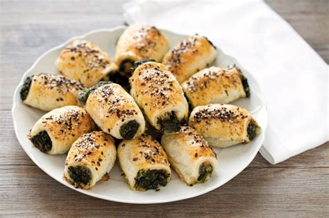 Preparazione di rustici salati con ripieno di spinaci e mozzarella su un tagliere di legno