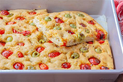 Immagine di una focaccia pugliese dorata e soffice, tagliata a fette, con pomodorini e olive.