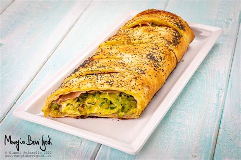 rotolo di pasta sfoglia con ripieno di spinaci, spennellato con uovo e cosparso di semi di sesamo, pronto per essere infornato