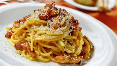 Primo piano di un piatto di birria pasta fumante, con rigatoni ben conditi, pezzi di carne sfilacciata e una generosa spolverata di formaggio fuso.