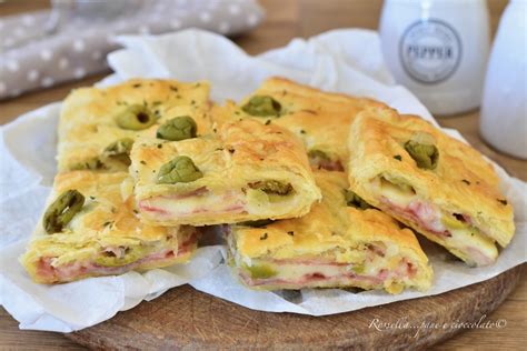 Rotoli di pasta sfoglia, prosciutto cotto a fette e mozzarella a cubetti disposti su un piano di lavoro.