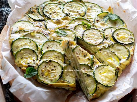padella con zucchine che stufano, contornate da erbe aromatiche e mandorle