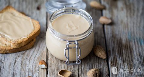 Vaso di crema di mandorle spalmata su pane integrale con alcune mandorle sparse attorno