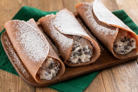 Necci al cioccolato aperti a metà, mostrando il ripieno di ricotta, zucchero a velo e gocce di cioccolato.