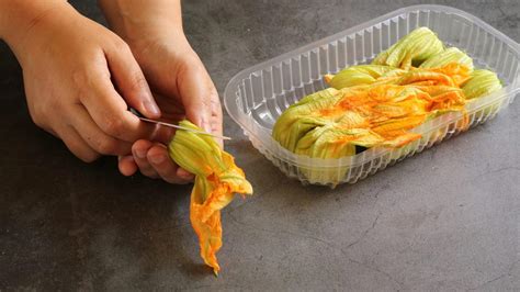 Primo piano di mani che puliscono delicatamente un fiore di zucca, rimuovendo il pistillo interno con uno strumento.