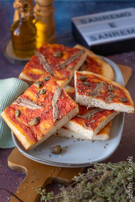 Immagine di una Sardenaira tagliata a quadrotti, con pomodoro, acciughe e olive