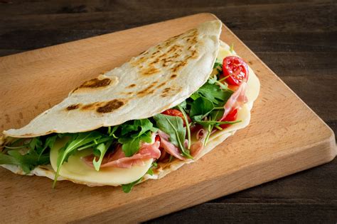 Primo piano di una piadina aperta che mostra la farcitura generosa di salsiccia sbriciolata, cipolle caramellate e peperoni arrostiti.