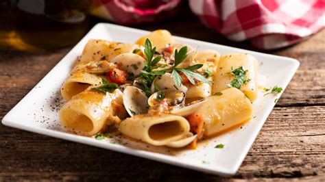 Primo piano di un piatto di paccheri con scampi e frutti di mare, guarnito con prezzemolo fresco.