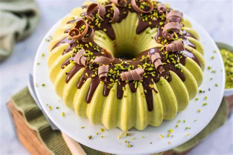Una fetta di bavarese al pistacchio su un piatto, con decorazioni di pistacchi tritati e riccioli di cioccolato.