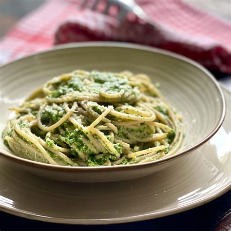 Piatto di spaghetti integrali con crema di spinaci e una spolverata di parmigiano.