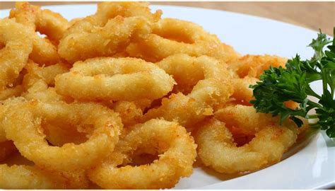 Anelli di calamari fritti croccanti e dorati su un piatto bianco, guarniti con spicchi di limone.