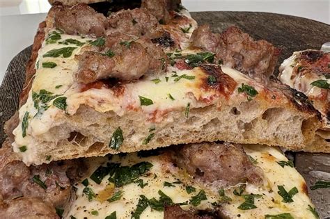 Immagine di una teglia di focaccia con stracchino e salsiccia, pronta per essere infornata
