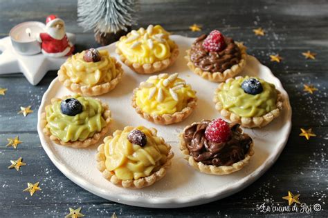 Un primo piano di tartellette finite, decorate con crema di caprino, prugne a spicchi, rigatino croccante e pinoli