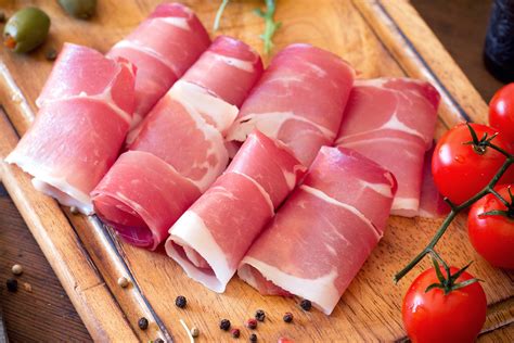 Fasi di preparazione di un involtino: spalmare il ripieno sul prosciutto crudo, arrotolare.