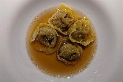 Immagine di ravioli serviti con una salsa scura e scaglie di formaggio.