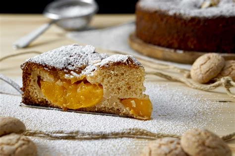 Una fetta di torta agli amaretti e pesche sciroppate su un piatto, con una spolverata di zucchero a velo