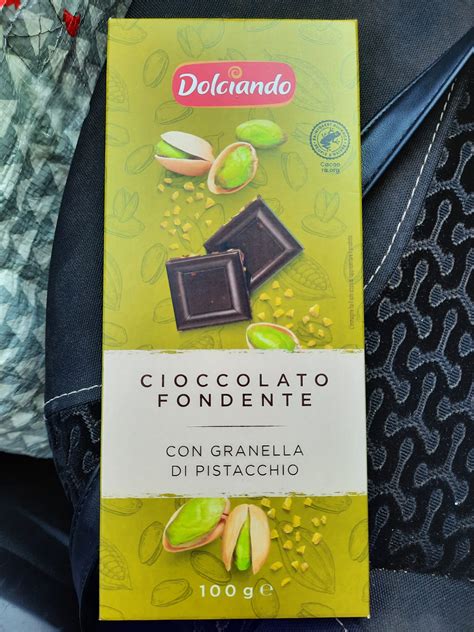 Inquadratura ravvicinata di una tortina al pistacchio ricoperta di cioccolato fondente, con granella di pistacchi e fleur de sel in evidenza.