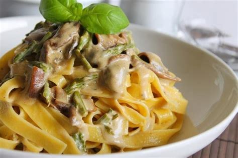 Piatto elegante di fettuccine all'uovo con panna, funghi porcini e asparagi