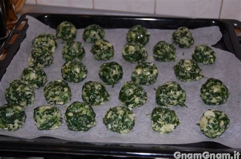 Polpette di merluzzo e spinaci disposte su una teglia pronte per la cottura al forno.
