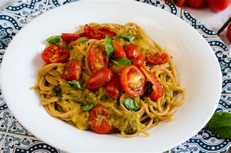 Primo piano di una porzione di pasta con tonno, zucchine e pomodorini, guarnita con basilico fresco