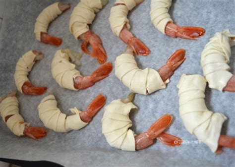 Gamberi avvolti in strisce di pasta sfoglia, con la coda visibile.