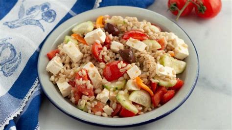 Immagine di una ciotola colorata di insalata di orzo greco con pollo e feta, pomodorini, cetrioli e olive.