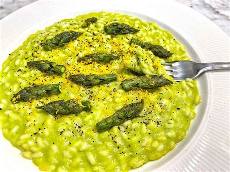 Primo piano di un risotto giallo zafferano con punte di asparagi come guarnizione