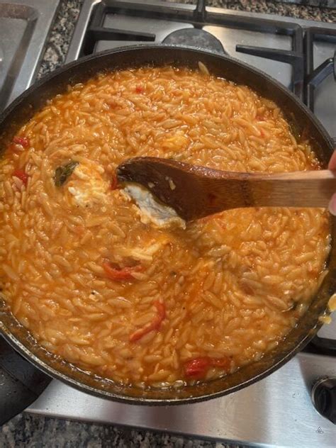 Una padella unica con risoni cremosi, pezzi di pollo e pomodoro, guarnita con basilico fresco.