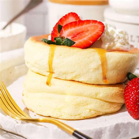 Una pila di soufflé pancake giapponesi decorati con panna montata e frutta fresca.