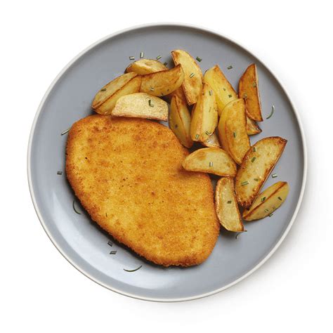 Immagine di una cotoletta impanata servita con patate al forno e un'insalata fresca