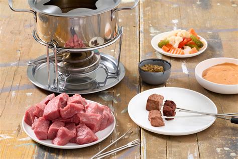 tavolo apparecchiato con tutto il necessario per la fondue bourguignonne: fornelletto, olio, carne, salse e forchette