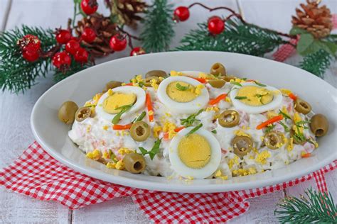 Una ciotola di insalata russa decorata con cetrioli a forma di albero di Natale e peperoni colorati come palline