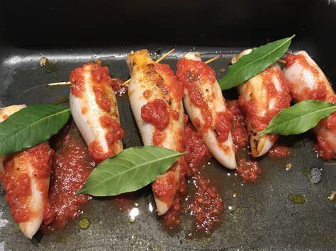 Immagine di calamari ripieni alla greca, pronti per essere serviti con contorno di pomodorini e rucola.
