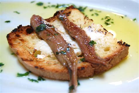 Immagine di un aperitivo con pane, burro e acciughe, accompagnato da bicchieri di bollicine.