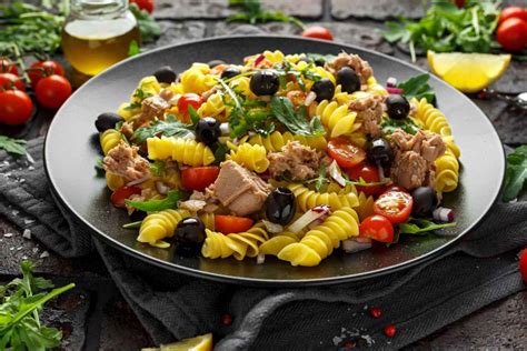 Primo piano di un piatto di pasta colorata con tonno, stracchino e basilico, decorato con pomodorini