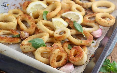 Anelli di calamari impanati dorati su una teglia da forno, accompagnati da spicchi di limone.