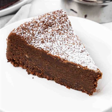 Una fetta di Torta Caprese con uno strato di marmellata d'albicocche visibile al centro, cosparsa di zucchero a velo.