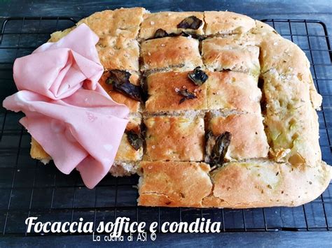 Focaccia cruda condita con zucchine affettate e mucchietti di crescenza su una teglia da pizza.