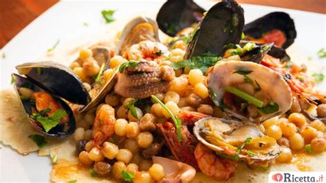 Primo piano di un piatto di fregola ai frutti di mare, con vongole, cozze e gamberi ben visibili, guarnito con prezzemolo fresco.