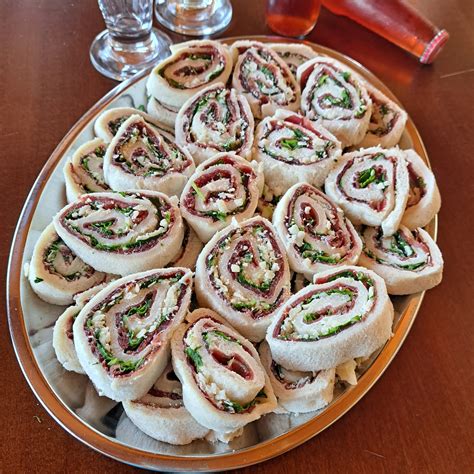 pane per tramezzini, bresaola, robiola spalmabile e rucola disposti su un piano di lavoro per la preparazione dei rotolini