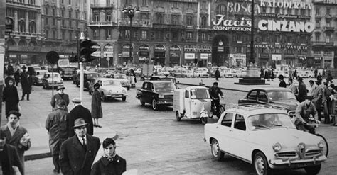 Scena d'epoca ambientata in una Milano degli anni '50, con auto d'epoca e architettura italiana
