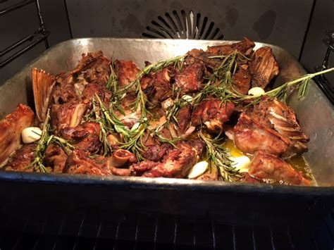 Capretto al forno su un piatto rustico, con erbe aromatiche e spicchi d'aglio.