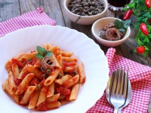Primo piano di un piatto di penne con capperi e alici