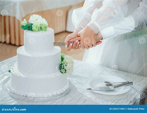 primo piano delle mani degli sposi che tagliano la torta nuziale con un coltello decorato