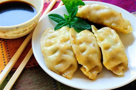 Un primo piano di ravioli cinesi al vapore serviti con una ciotolina di salsa di soia e decorati con cipollotto fresco.