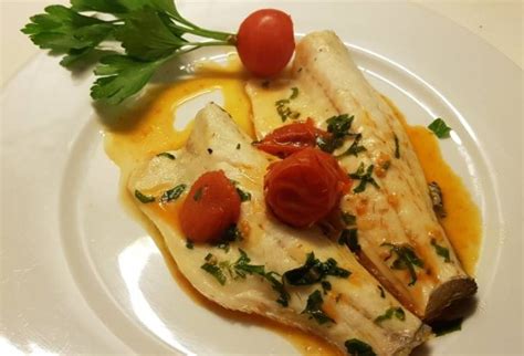 Immagine di un branzino succoso cotto alla piastra, con una leggera doratura e guarnito con erbe aromatiche.